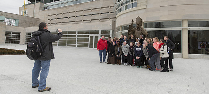 Pilgrims pose with the bronze statue of Pope John Paul II
